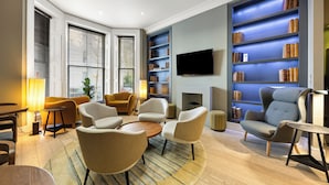 A modern living room with a fireplace, comfortable seating, a bookshelf, and a flat-screen TV. - Kula London Kensington (London)