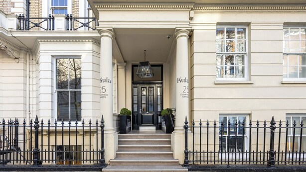 A building entrance with a set of steps leading to a door, flanked by two columns and a black iron fence. - Kula London Kensington (London)