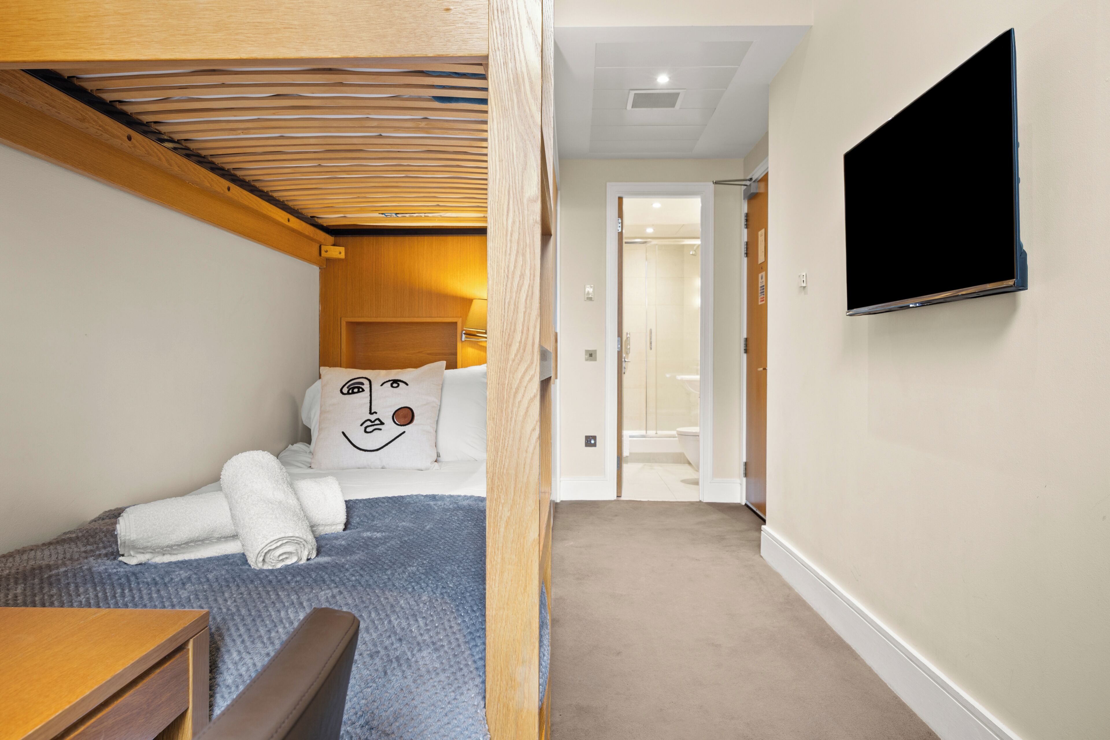 A bedroom with a bunk bed, a flat-screen TV, a wooden headboard, and a bathroom visible through an open door.