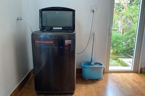 A compact, dark-colored refrigerator with a water dispenser, connected to a blue water fountain, and a power outlet on the wall. - Tuong Vy Villa (Dalat)