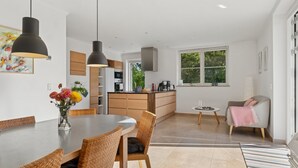 A modern kitchen with wooden cabinets, a dining area with wicker chairs, and a view of the outdoors through a large window. - "Alvia" - 1.6km from the sea by Interhome (Græsted)