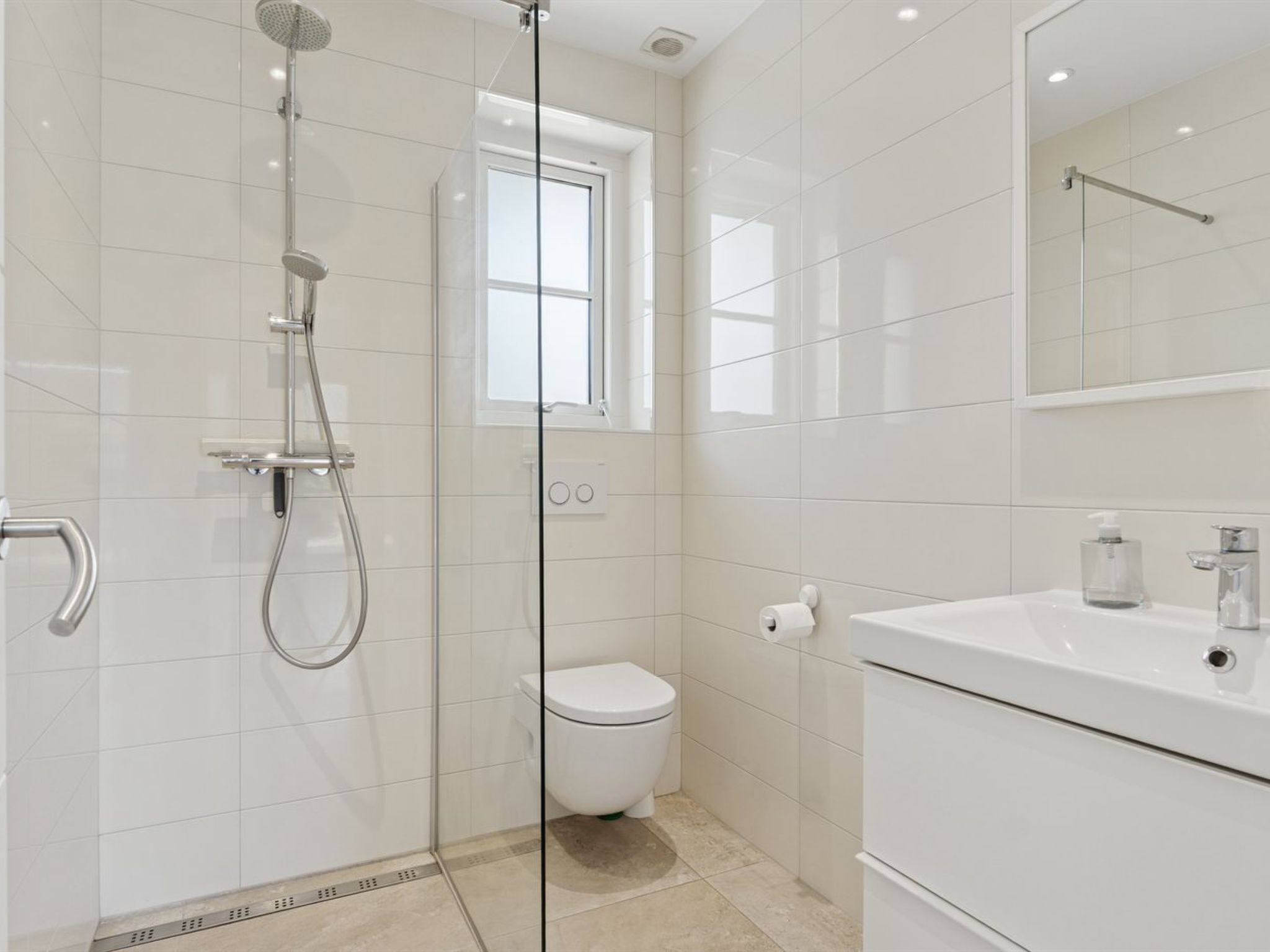 A modern bathroom with a glass-enclosed shower, a toilet, and a sink with a mirror above.