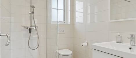 A modern bathroom with a glass-enclosed shower, a toilet, and a sink with a mirror above.