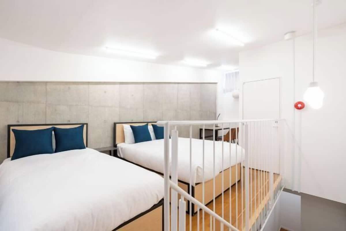 A room with two beds, a concrete headboard, white walls, and a wooden floor.