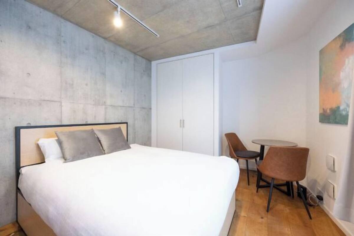 A bedroom with a bed, a wardrobe, a dining table with chairs, and a painting on the wall.