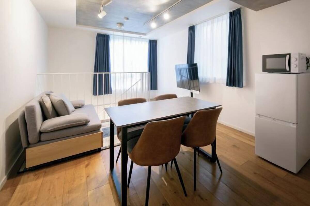 A compact living space with a sofa, dining table, chairs, a TV, and a refrigerator.