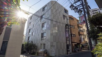 A multi-story building with a geometric facade, a visible trash bin, and a street with a clear sky.