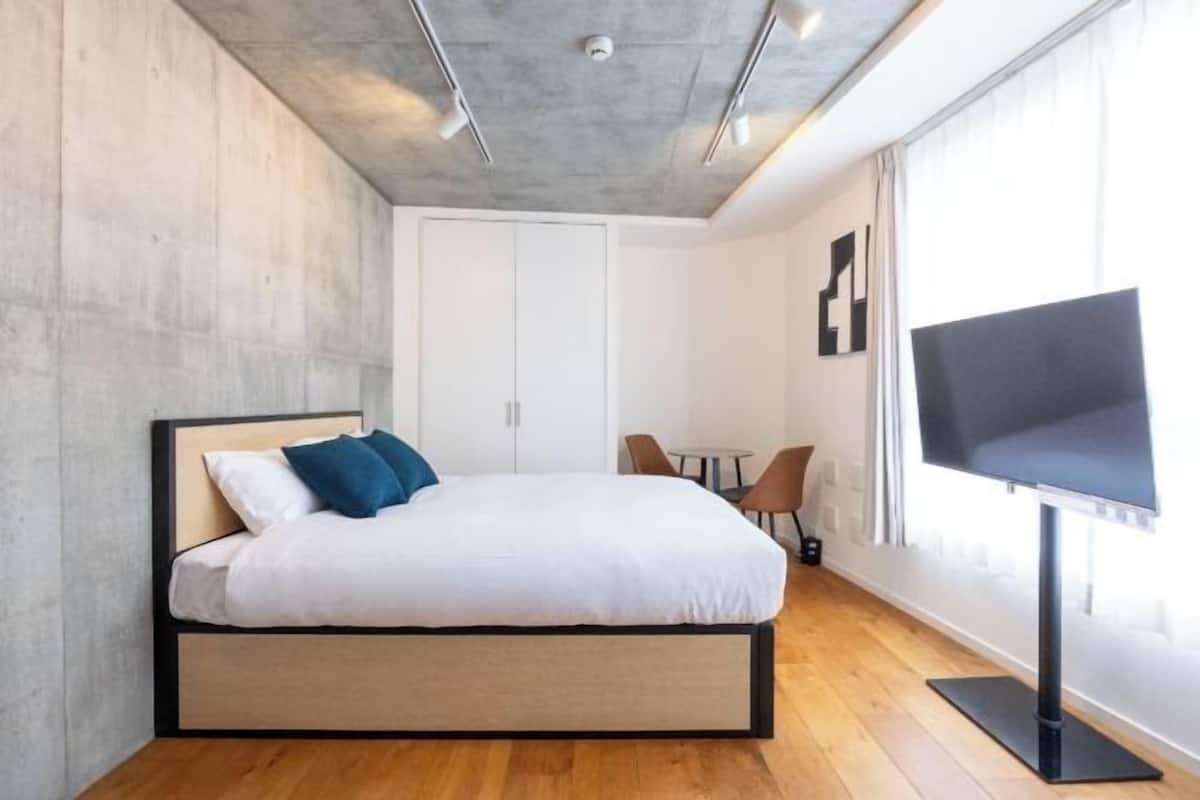A modern bedroom with a bed, a TV, a desk, and a chair.