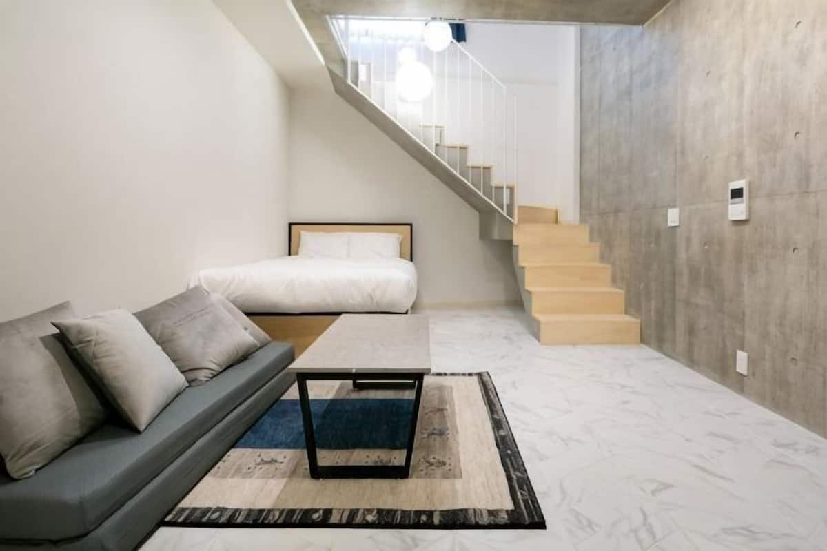 A modern living room with a sofa, a coffee table, a rug, a staircase, and a concrete wall.