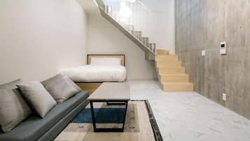 A modern living room with a sofa, a coffee table, a rug, a staircase, and a concrete wall.