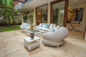A modern outdoor seating area with a white sofa, a round table, and a decorative bird sculpture. - OMEKAI Cemagi by Nakula (Bali)
