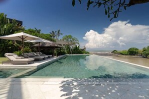A swimming pool with lounge chairs and umbrellas, a clear view of the sea, and a tropical landscape. - OMEKAI Cemagi by Nakula (Bali)
