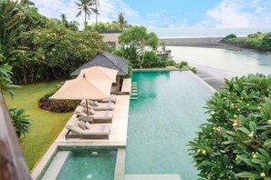 A pool area with lounge chairs and umbrellas, surrounded by lush greenery and a view of the ocean. - OMEKAI Cemagi by Nakula (Bali)