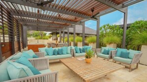 An outdoor patio with a wooden table and cushioned seating, surrounded by greenery and a pergola structure. - OMEKAI Cemagi by Nakula (Bali)