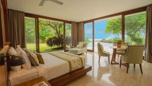 A bedroom with a bed, a desk, and a chair, large windows with a view of greenery and the sea. - OMEKAI Cemagi by Nakula (Bali)