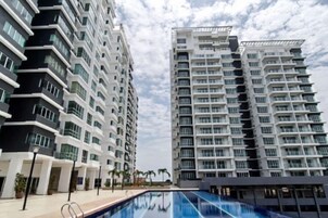 Un edificio residencial moderno con piscina, varios balcones y cielo despejado.