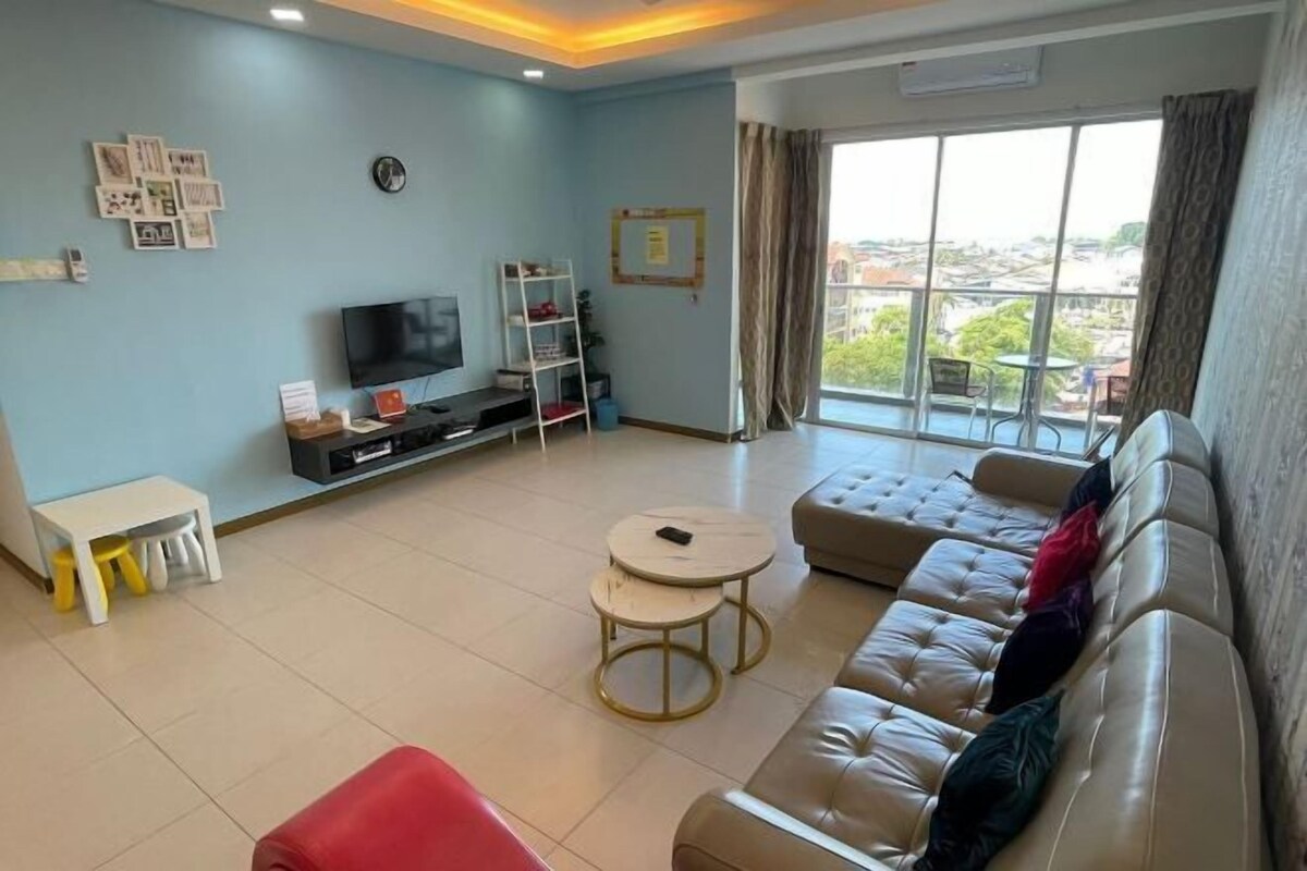 Ein Wohnzimmer mit einer großen Couch, einem Fernseher, einem kleinen Tisch und einem Fenster mit Blick.
