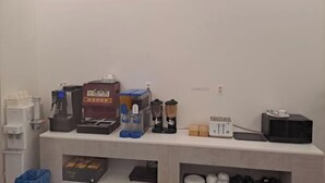 Una kitchenette equipada con cafetera, licuadora, tostadora y diversos recipientes.