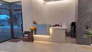 Zona de recepción con puerta de cristal, mostrador de recepción, un taburete pequeño y una planta.