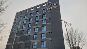 Un moderno edificio de hotel con varios pisos, ventanas amplias y un letrero destacado que dice "LA SCENE HOTEL".