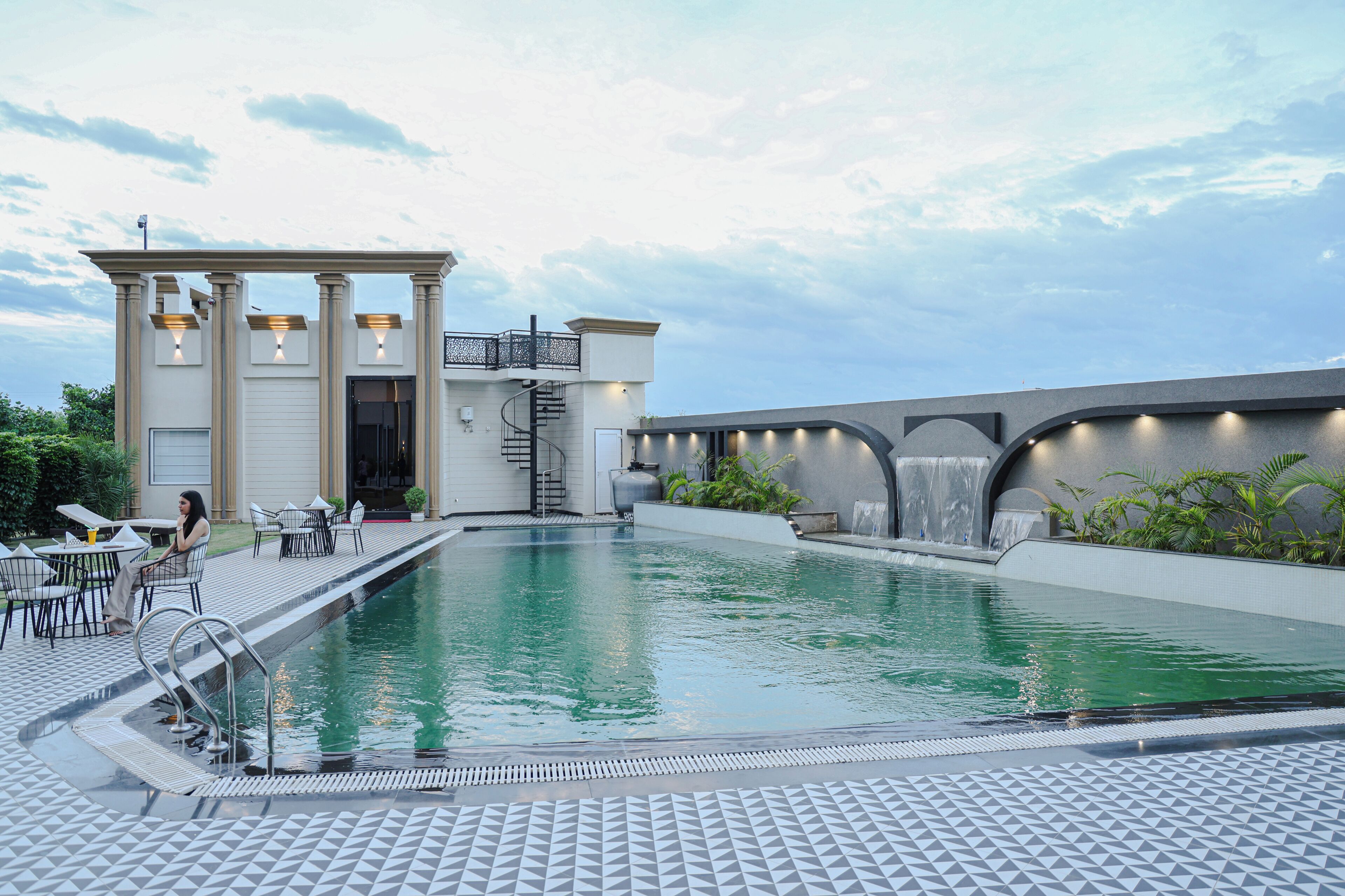 A swimming pool with a modern design, a covered seating area, and a water feature.