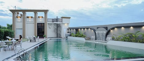A swimming pool with a modern design, a covered seating area, and a water feature.