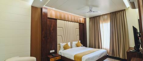 A hotel room with a bed, a desk, a chair, a TV, and a ceiling fan.