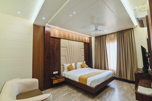 Quarto de hotel com uma cama, escrivaninha, cadeira, televisão e ventoinha no teto.