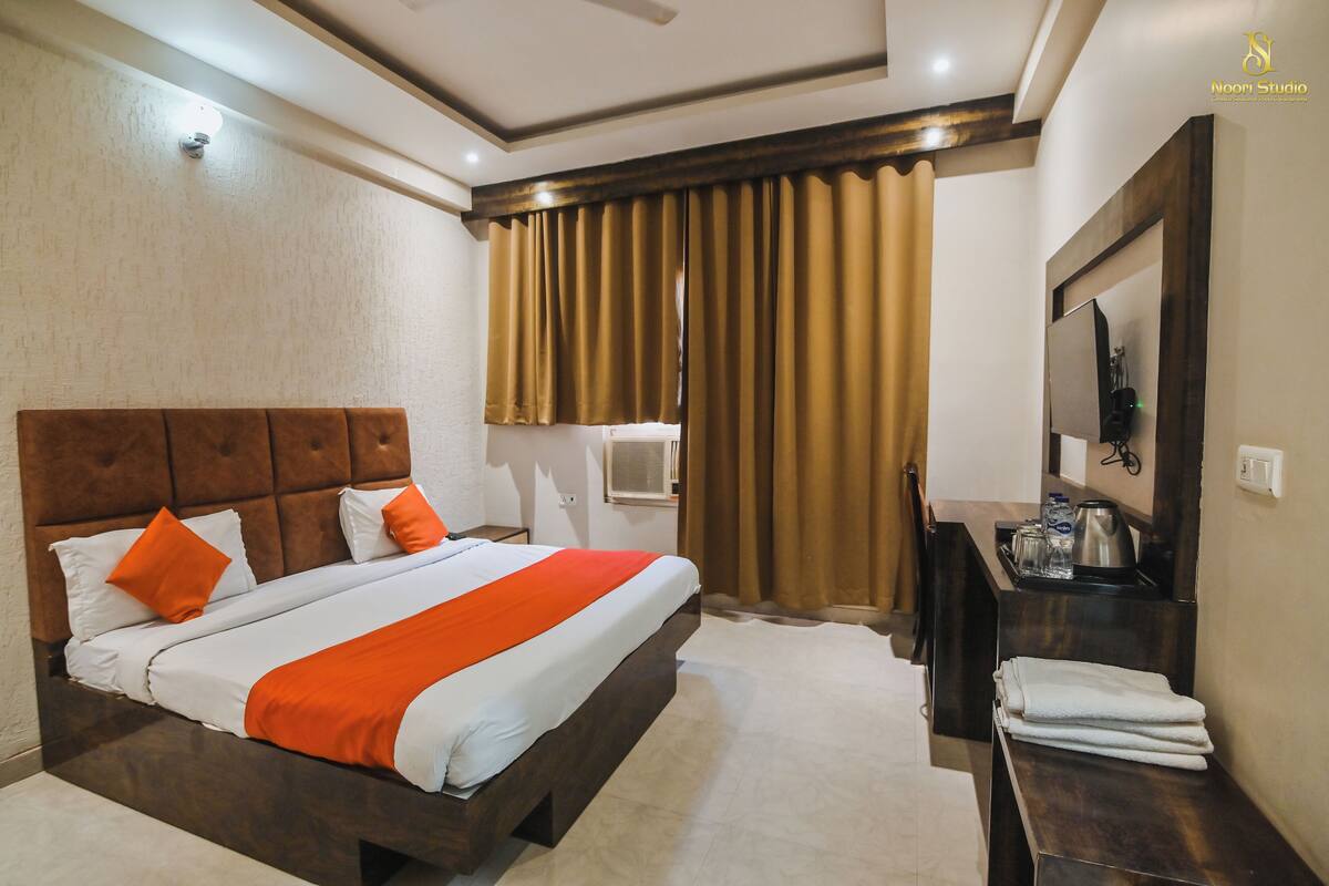 Quarto de hotel com cama, escrivaninha, televisão e janela com cortinas.