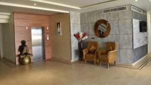 Un hall con mostrador de recepción, dos sillones, una estatua de Buda, un espejo en la pared y un moderno ascensor.