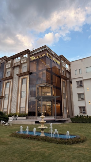 Een modern hotel met een opvallende ingang, een decoratieve fontein en een verzorgd gazon.