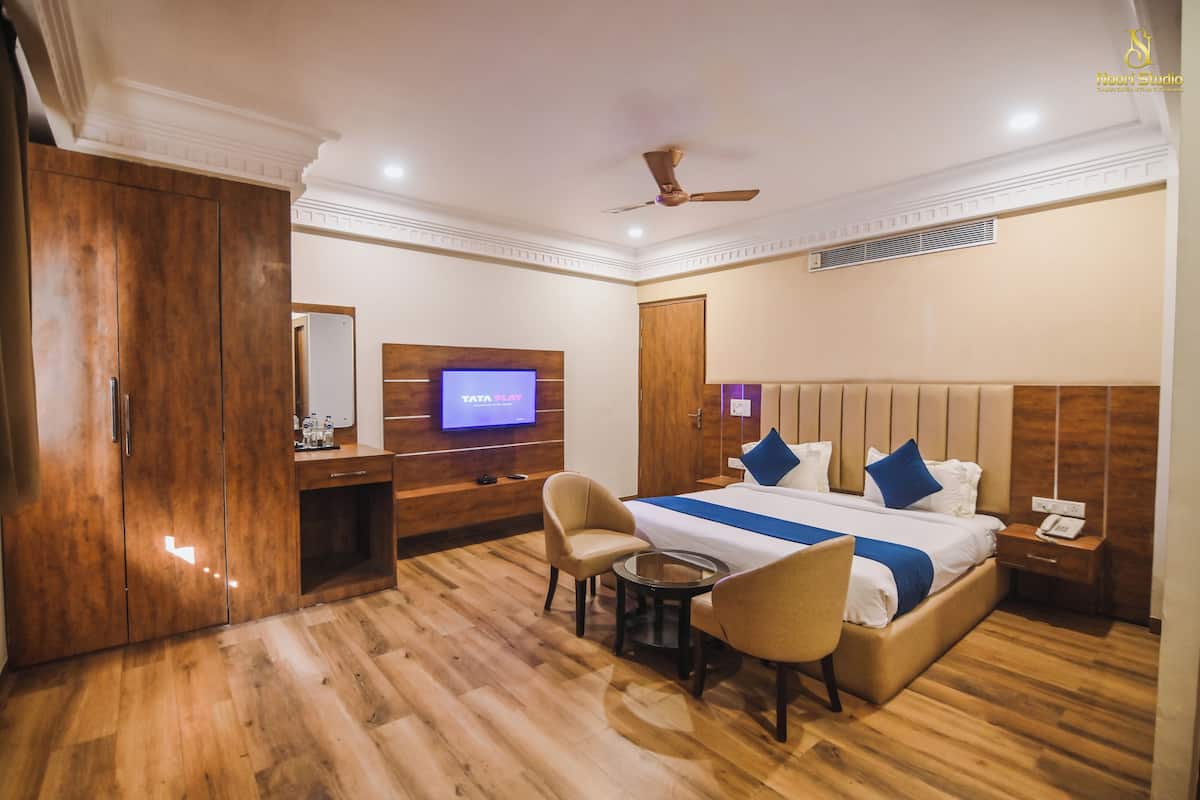 Quarto de hotel com cama, escrivaninha, televisão, cadeira e mesa pequena.