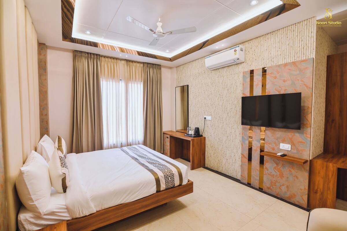 Quarto de hotel com cama, escrivaninha, televisão e ar condicionado.
