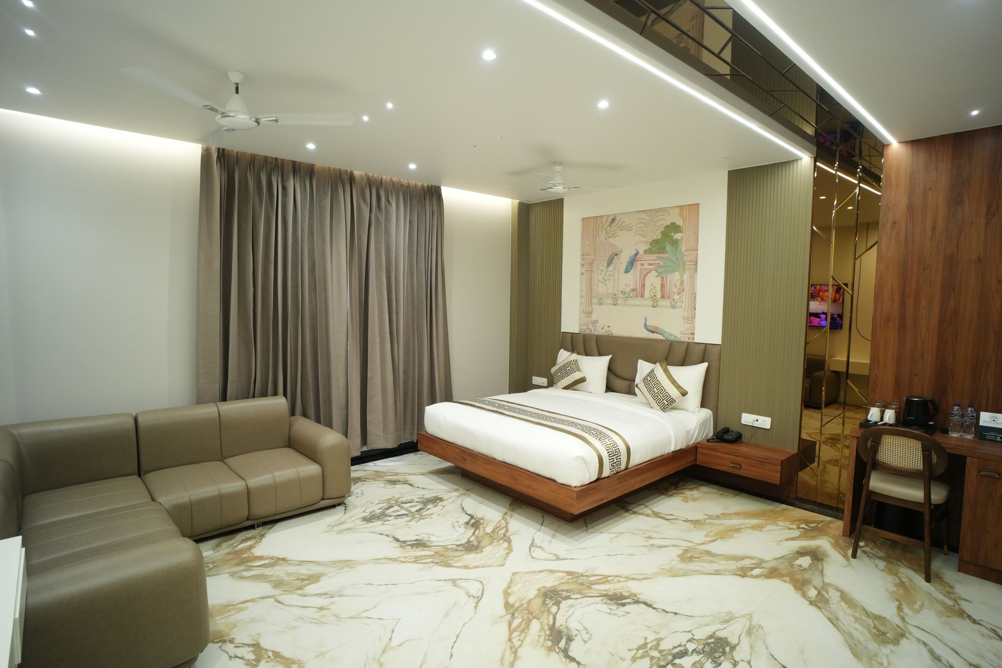A modern hotel room with a bed, a sofa, a desk, and a painting on the wall.