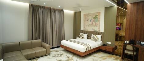 A modern hotel room with a bed, a sofa, a desk, and a painting on the wall.