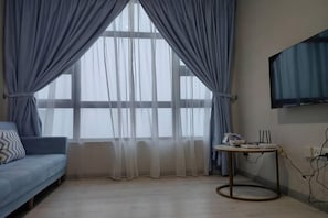 A room with a sofa, a small table, a TV mounted on the wall, and a window with curtains. - The Loft Imago Shopping Mall By Chill Time (Kota Kinabalu)