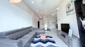 A modern living room with a grey sectional sofa, a small round table, a flat-screen TV, and a ceiling fan. - The Loft Imago Shopping Mall By Chill Time (Kota Kinabalu)