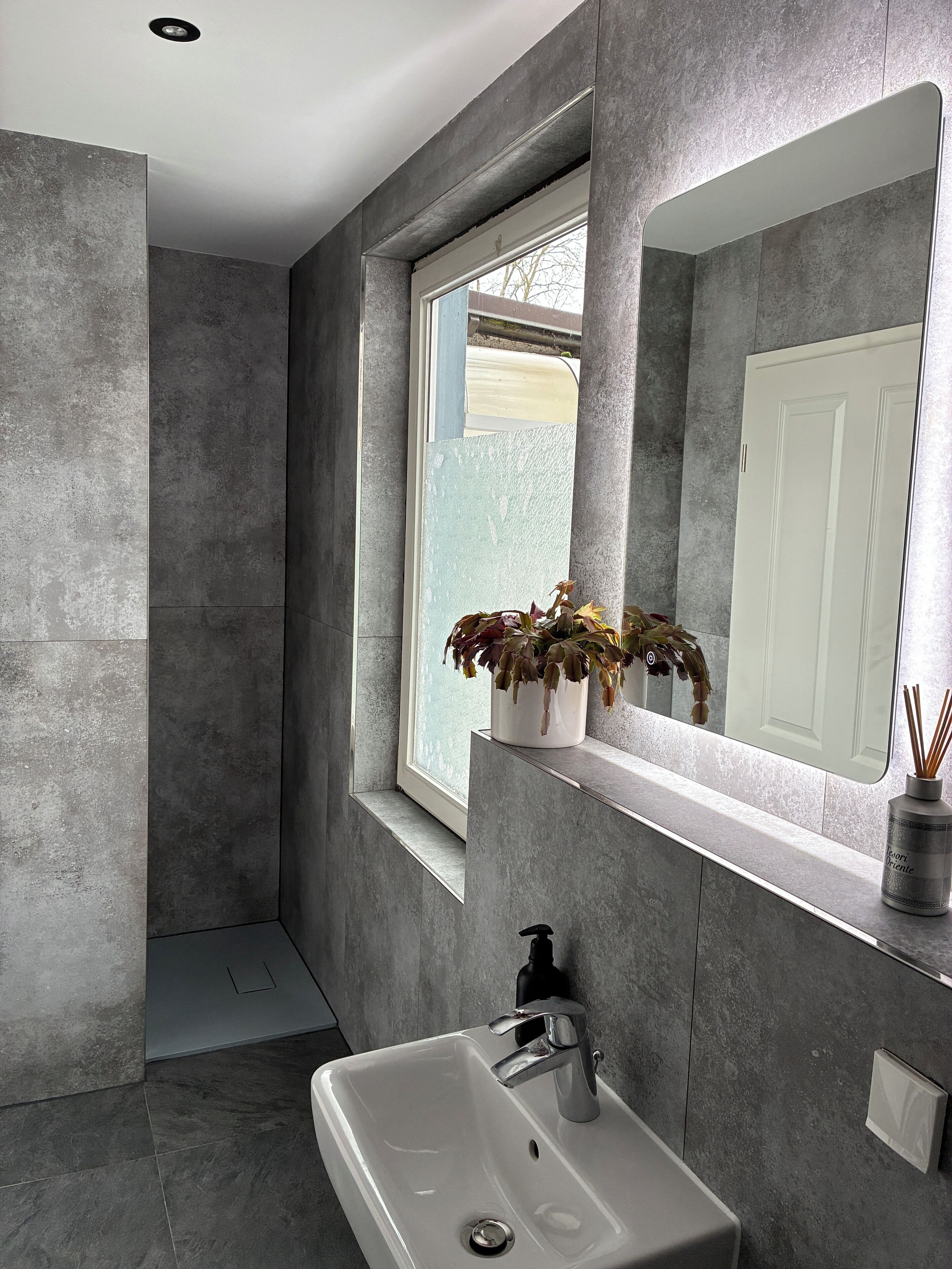 Une salle de bain moderne avec un grand miroir, un lavabo et une fenêtre agrémentée de plantes.
