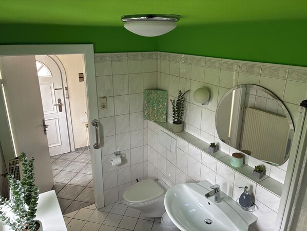 A bathroom with a toilet, sink, and mirror, featuring green walls and white tiles.