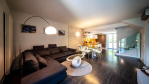 Ein modernes Wohnzimmer mit einem dunkelbraunen Ecksofa, einem runden Couchtisch und einem Essbereich mit einem Glastisch und weißen Stühlen.