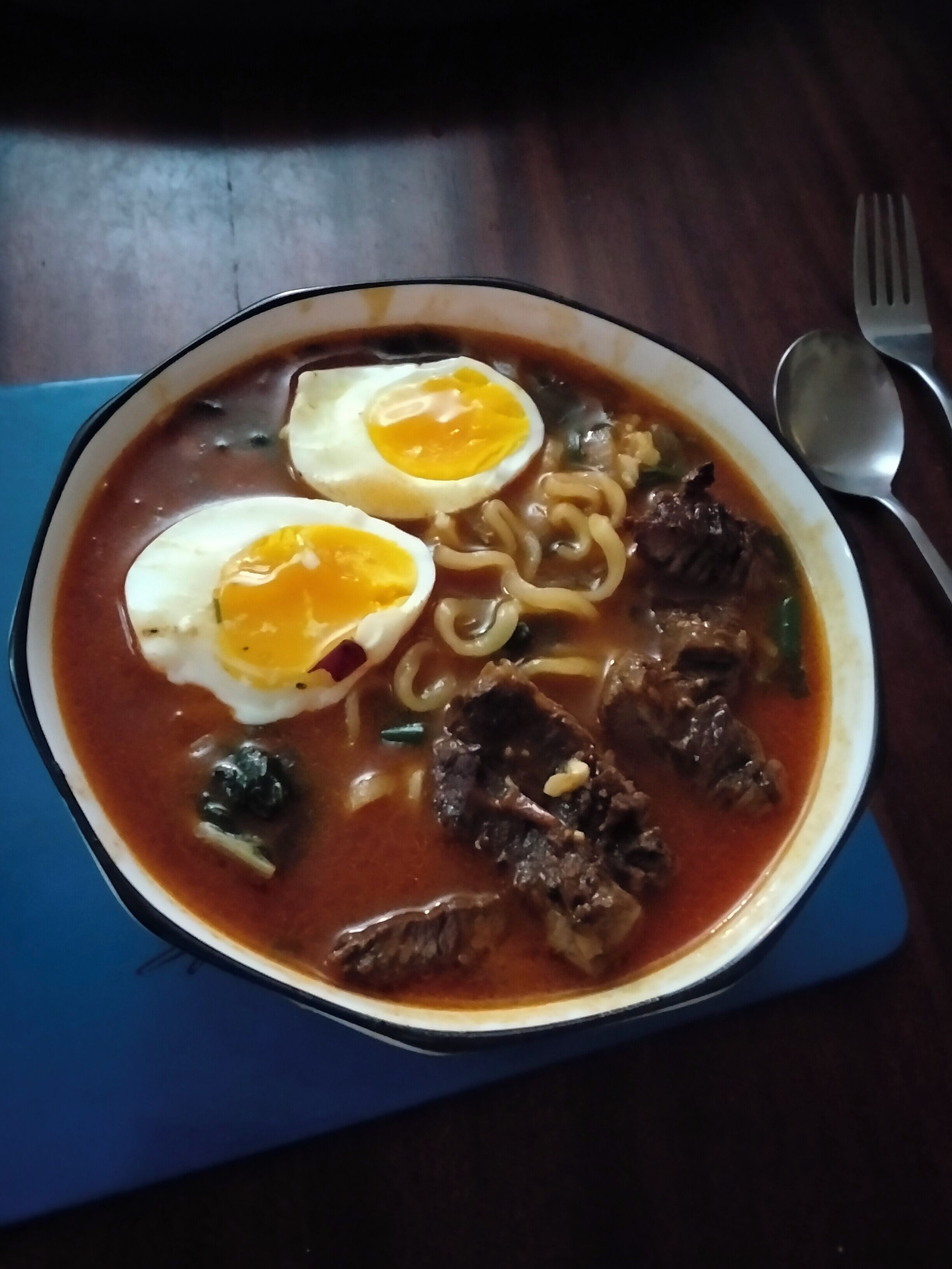 Un tazón de ramen con lonjas de carne, fideos y dos mitades de huevo cocido.