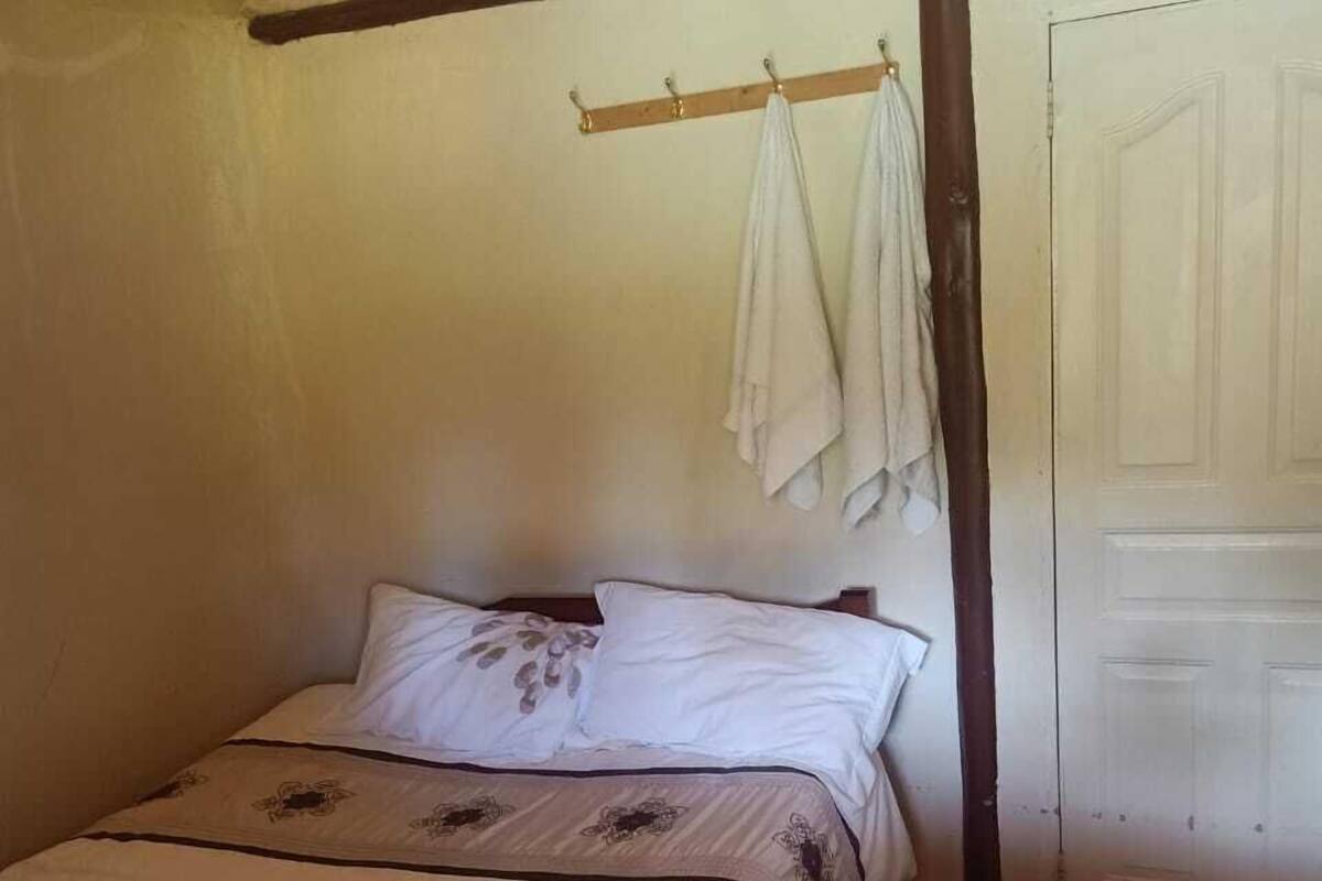 A single bed with a floral-patterned bedspread, a wooden headboard, a small table, and a white door.