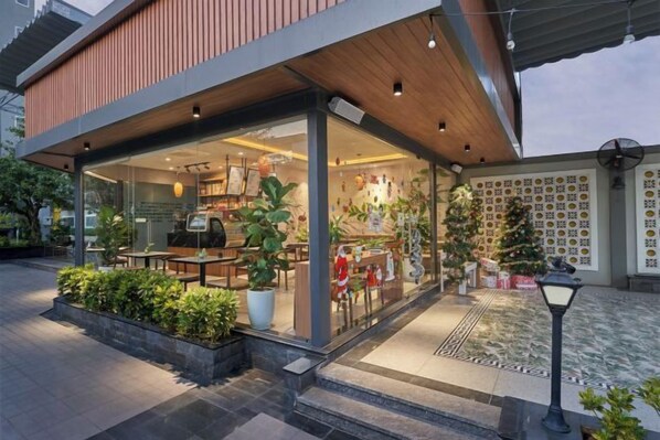 A modern building with a covered outdoor seating area, a coffee shop inside, and a decorative wall with patterns. - Bcons PS Bien Hoa Hotel (Bien Hoa)