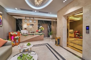 A hotel reception area with a marble counter, a receptionist, and a modern chandelier. - Bcons PS Bien Hoa Hotel (Bien Hoa)