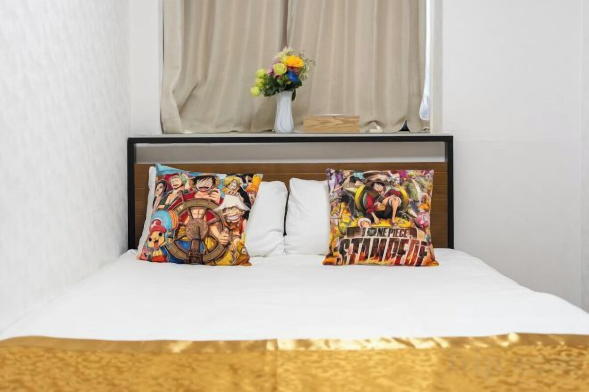 Een bed met twee kleurrijke kussens, een vaas met bloemen en een raam met gordijnen.
