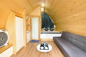 Una camera accogliente con soffitto in legno, un divano, un piccolo tavolo con vassoio e un letto con cuscini.
