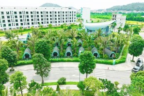 A modern hotel with multiple green-roofed structures, a central building with a curved facade, and a surrounding landscaped area with trees. - Xanh Melody Resort (Viet Doan)