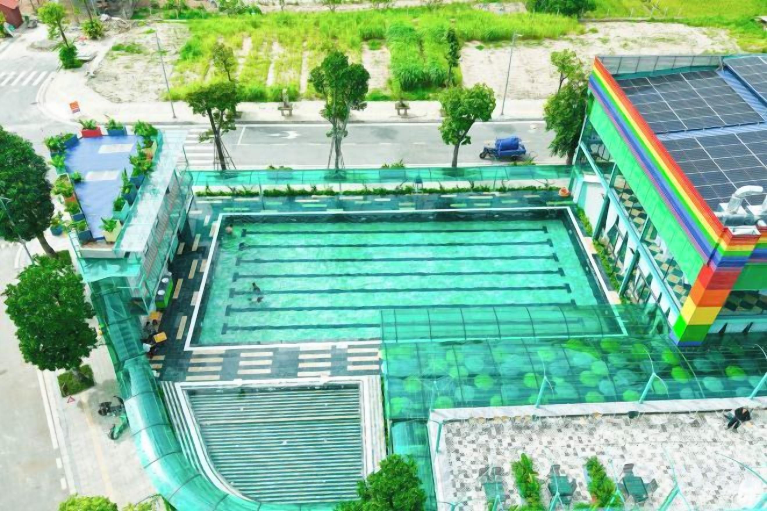 Une piscine entourée d’une terrasse, un espace abrité et un bâtiment dont le toit est recouvert de panneaux solaires.