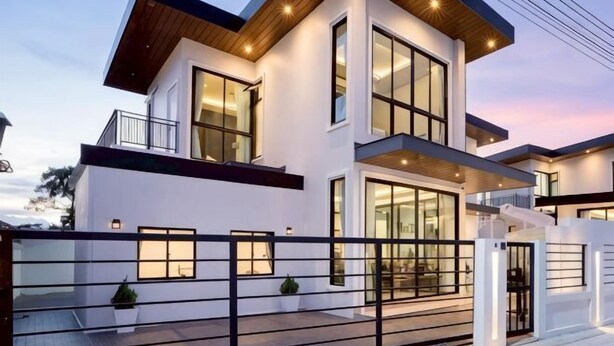 Una casa moderna de dos pisos con ventanas amplias, un balcón y un acceso con reja.