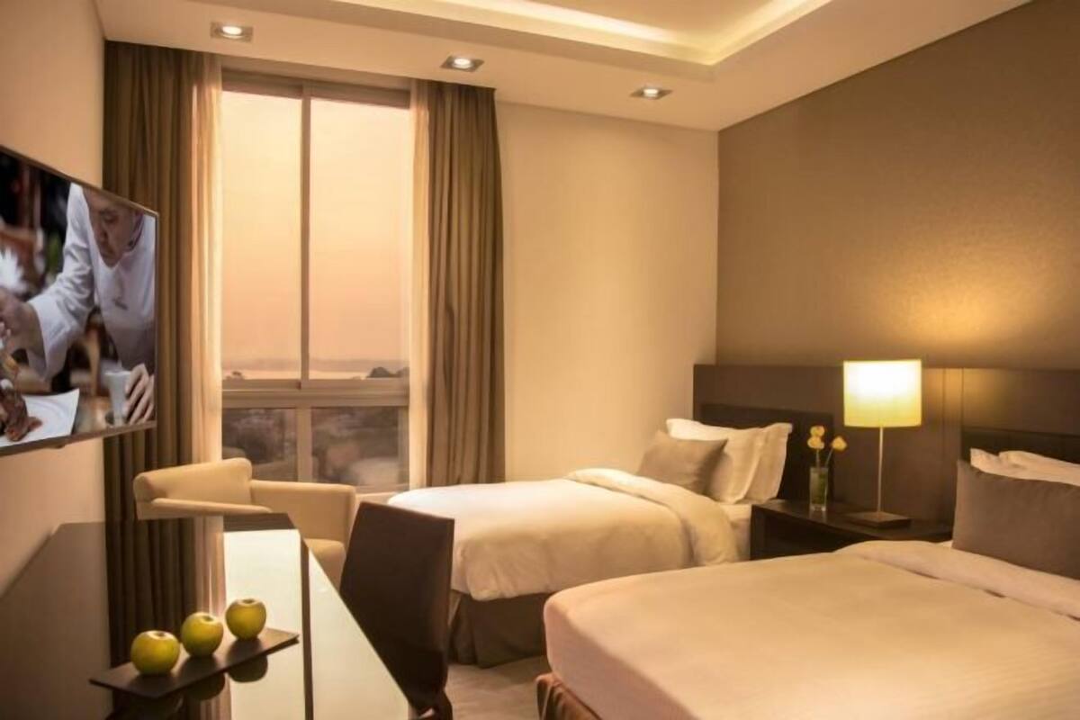 Ein Hotelzimmer mit zwei Betten, einem Schreibtisch, einem Stuhl, einem Fernseher und einem Fenster mit Vorhängen.